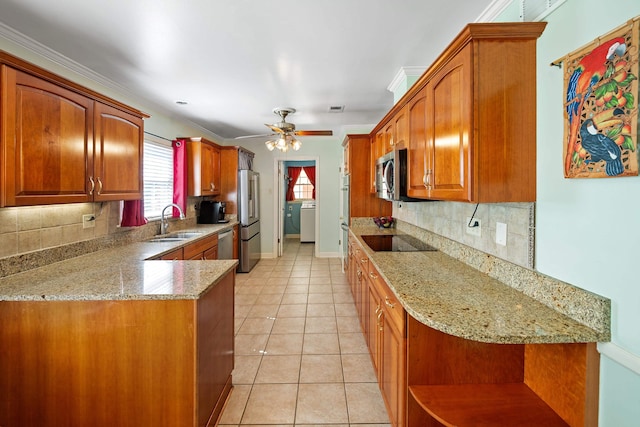 kitchen with ceiling fan, brown cabinetry, appliances with stainless steel finishes, light stone countertops, and a sink