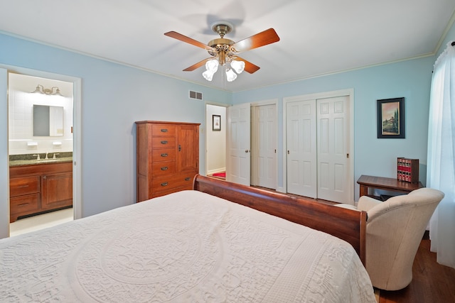 bedroom featuring visible vents, multiple closets, wood finished floors, connected bathroom, and a sink