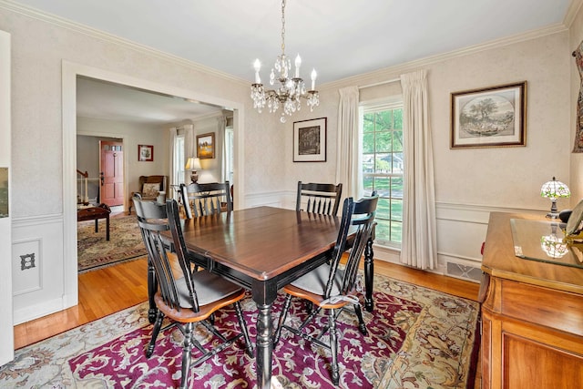 dining area featuring a notable chandelier, light wood-style floors, a wainscoted wall, visible vents, and ornamental molding