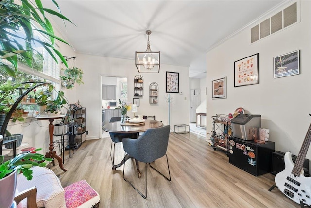 dining space featuring ornamental molding, a notable chandelier, light wood finished floors, and visible vents