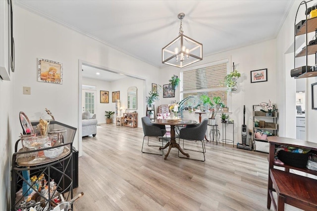 dining room with an inviting chandelier, ornamental molding, and light wood-style flooring