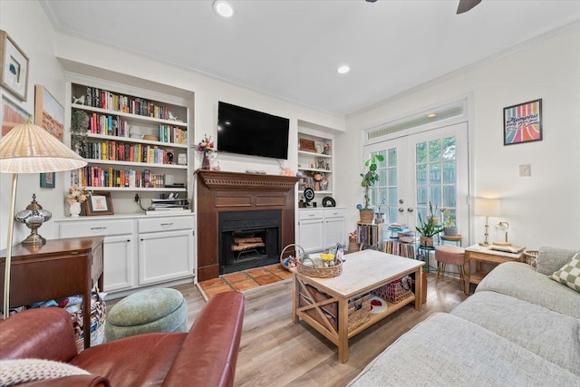 living area with crown molding, a fireplace, built in features, french doors, and light wood-style flooring