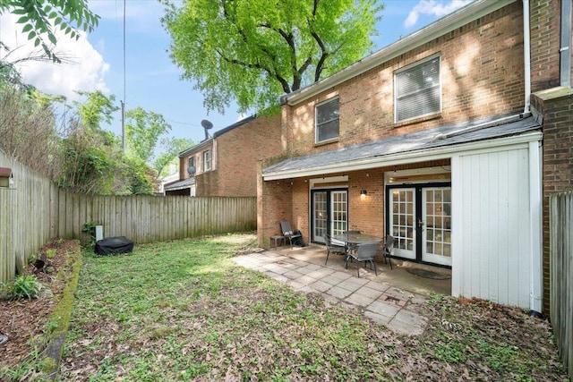rear view of house featuring brick siding, french doors, a fenced backyard, and a patio area