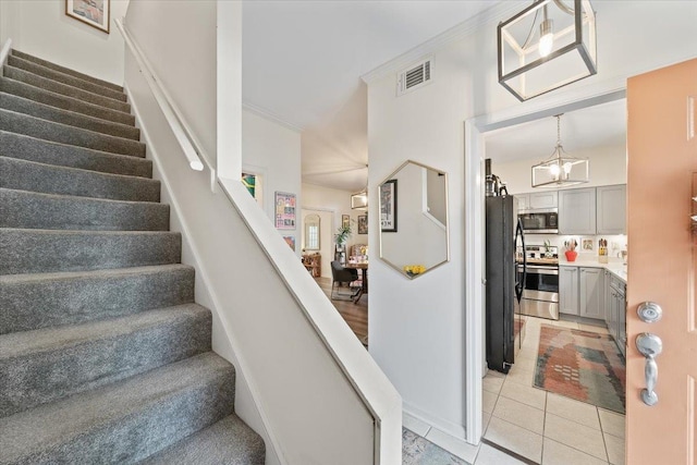 staircase featuring visible vents, crown molding, tile patterned floors, and a chandelier