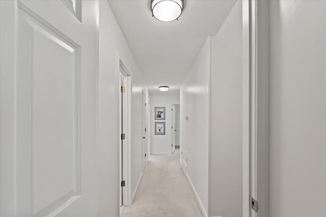 hallway featuring baseboards and light carpet
