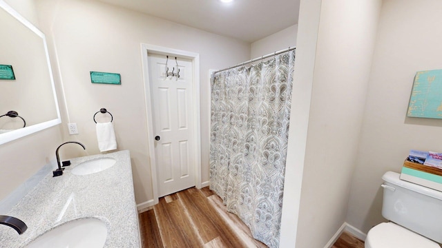 full bathroom with a sink, double vanity, toilet, and wood finished floors