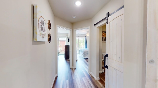 corridor with baseboards, a barn door, and wood finished floors