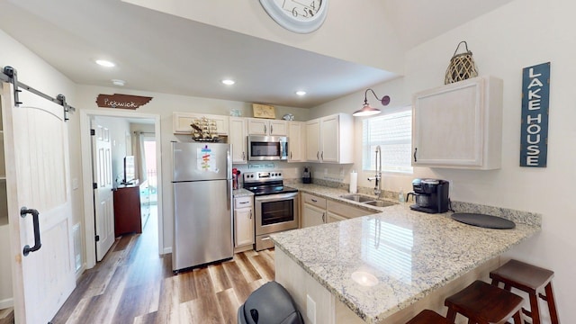 kitchen with a sink, light wood finished floors, a peninsula, a breakfast bar, and stainless steel appliances