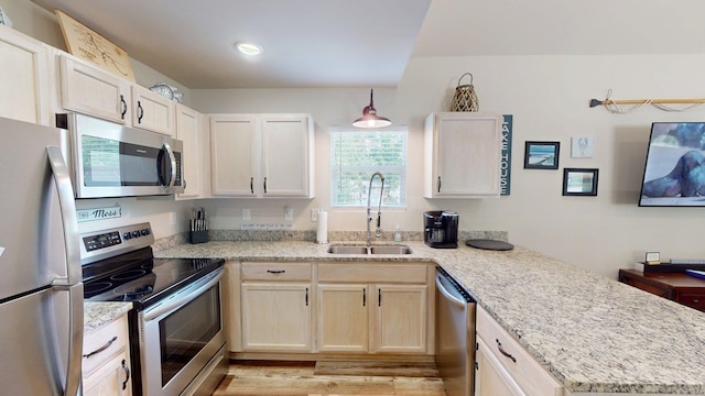 kitchen with light stone countertops, a sink, a peninsula, light wood-style floors, and stainless steel appliances