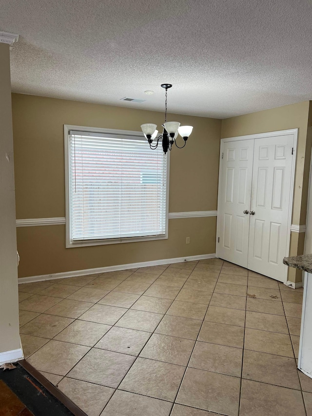 unfurnished dining area featuring an inviting chandelier, light tile patterned floors, plenty of natural light, and a textured ceiling