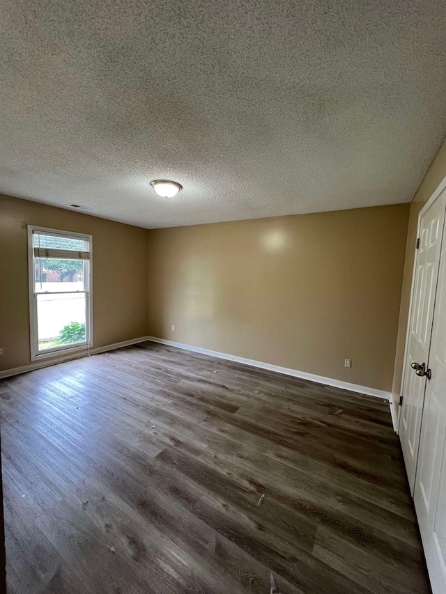 spare room featuring baseboards, a textured ceiling, dark wood-style floors, and visible vents