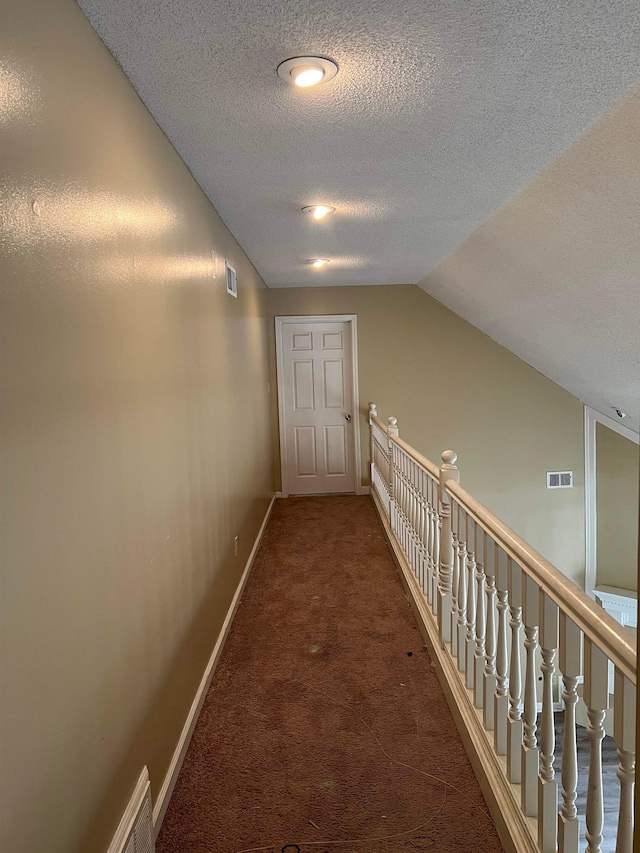 hallway with a textured ceiling, visible vents, baseboards, and carpet