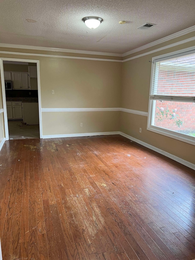 empty room featuring a textured ceiling, visible vents, ornamental molding, and hardwood / wood-style floors