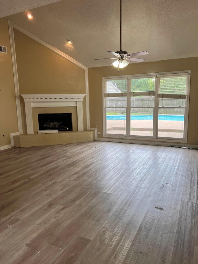 unfurnished living room featuring a fireplace with raised hearth, a textured ceiling, ceiling fan, and wood finished floors