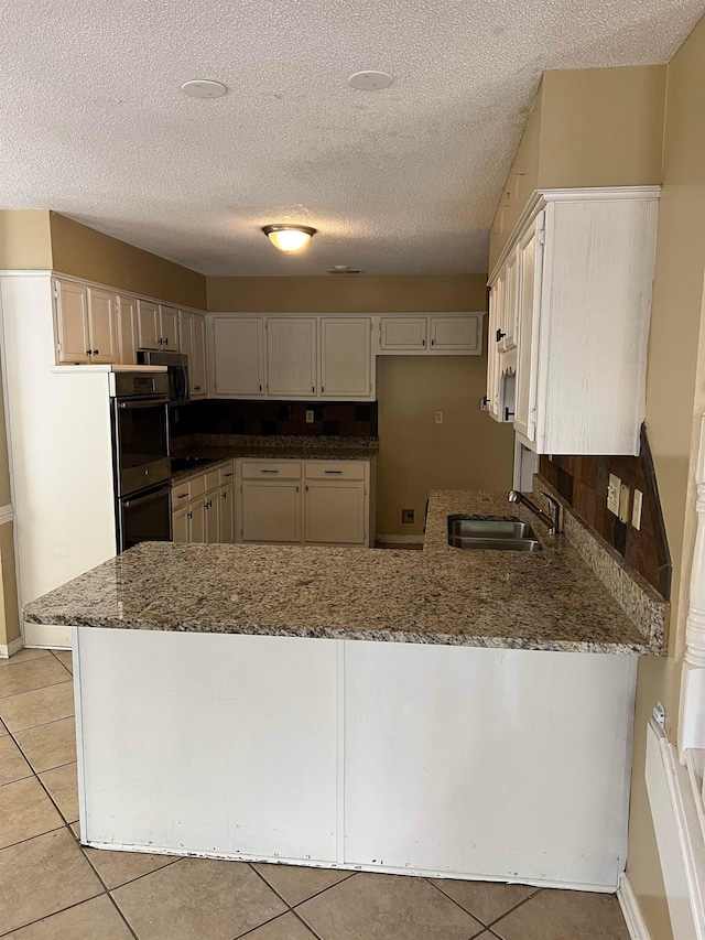 kitchen with light tile patterned flooring, a sink, dark stone counters, a peninsula, and stainless steel appliances