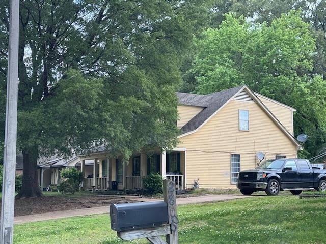 view of side of property with covered porch, a lawn, and a shingled roof