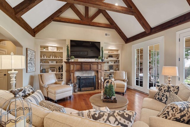living area featuring visible vents, built in shelves, wood finished floors, beam ceiling, and high vaulted ceiling