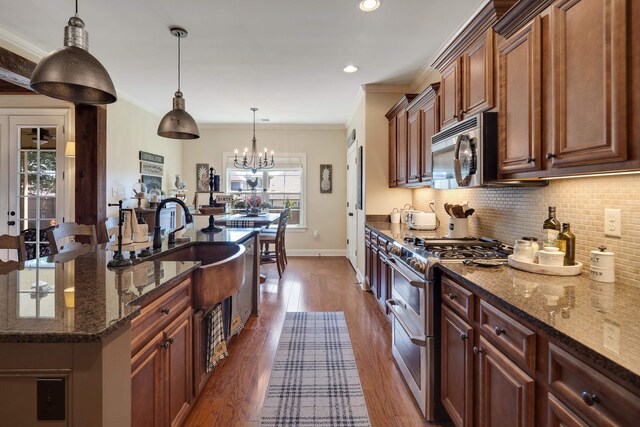 kitchen with crown molding, appliances with stainless steel finishes, a sink, baseboards, and decorative backsplash