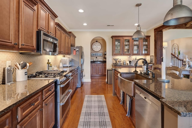 kitchen with appliances with stainless steel finishes, a sink, arched walkways, tasteful backsplash, and visible vents