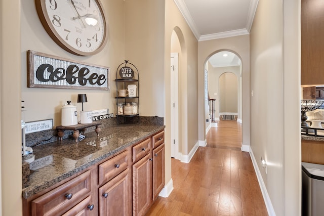 bar featuring crown molding, arched walkways, baseboards, and light wood-style flooring