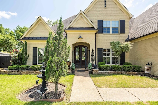 view of front of house featuring brick siding, a front lawn, french doors, and a standing seam roof