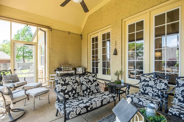 sunroom / solarium featuring brick wall, ceiling fan, and french doors