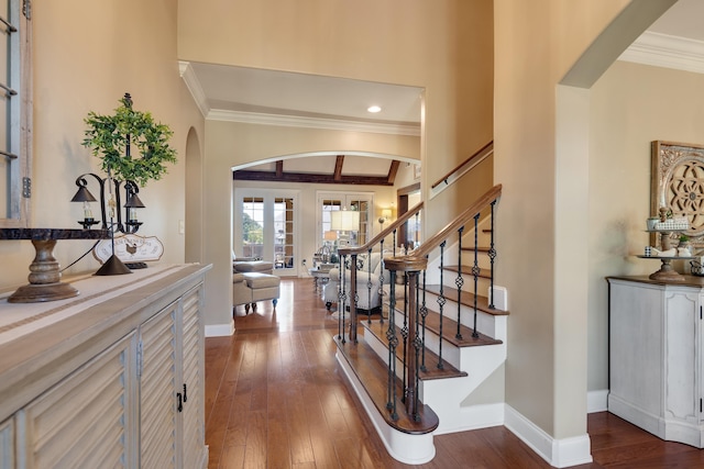 foyer entrance featuring dark wood-style flooring, crown molding, arched walkways, baseboards, and stairs