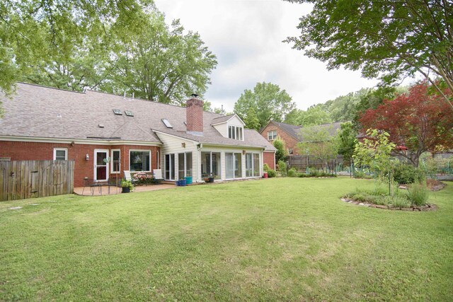 rear view of property featuring fence, a chimney, brick siding, a patio area, and a yard
