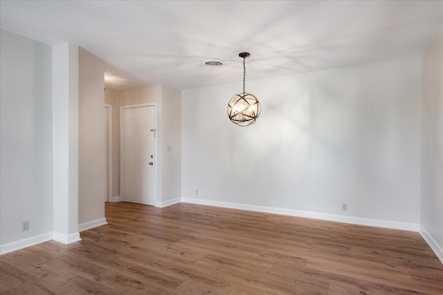 unfurnished dining area with an inviting chandelier, baseboards, wood finished floors, and visible vents