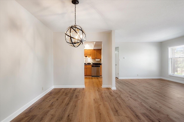 unfurnished dining area featuring baseboards, a chandelier, and light wood finished floors