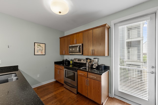 kitchen featuring brown cabinets, dark wood-style flooring, dark stone counters, stainless steel appliances, and baseboards