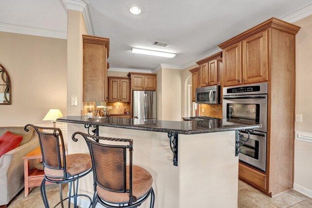 kitchen with a kitchen breakfast bar, crown molding, appliances with stainless steel finishes, tasteful backsplash, and a peninsula