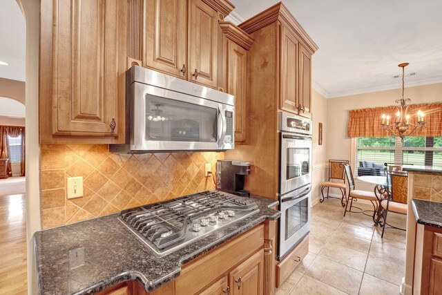 kitchen with decorative backsplash, crown molding, appliances with stainless steel finishes, arched walkways, and an inviting chandelier
