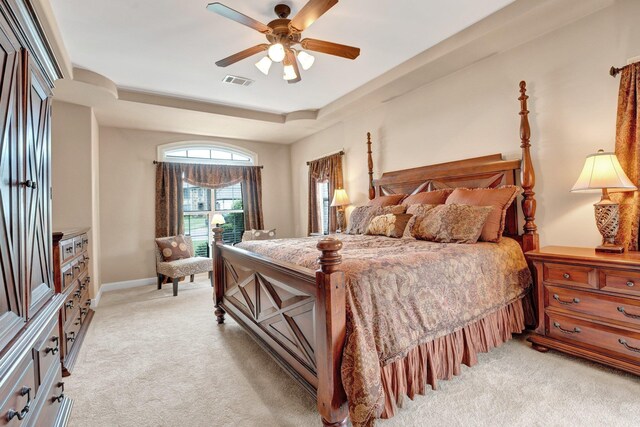 bedroom featuring light colored carpet, a ceiling fan, visible vents, and a raised ceiling