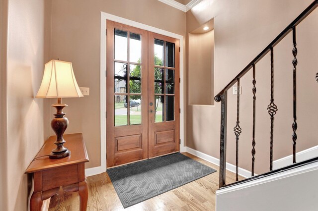 foyer entrance with crown molding, french doors, baseboards, wood finished floors, and stairway