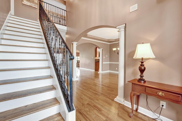 staircase with ornate columns, arched walkways, baseboards, and wood finished floors