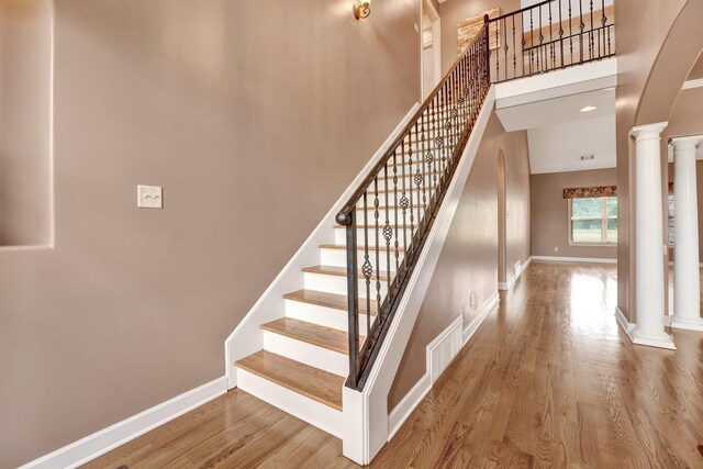 staircase with a towering ceiling, wood finished floors, baseboards, ornate columns, and arched walkways