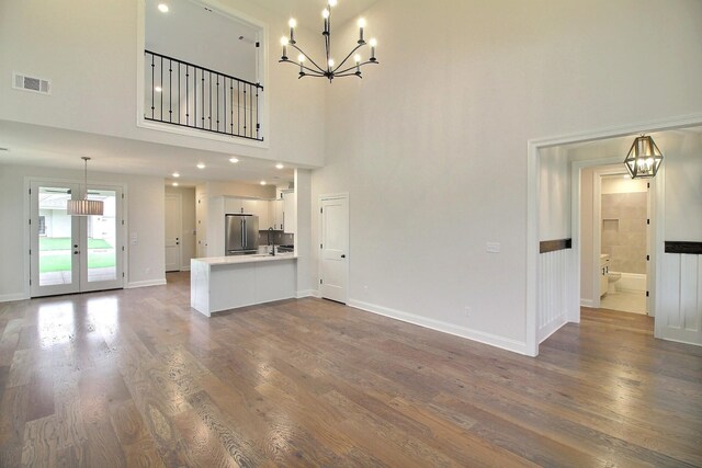 235 Freedom Ln, Rossville, TN 38066 - unfurnished living room featuring visible vents, wood finished floors, baseboards, a notable chandelier, and a high ceiling