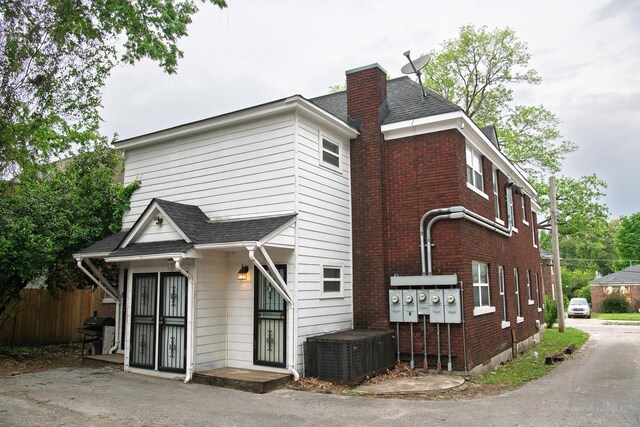 exterior space featuring a shingled roof, a chimney, central AC, and brick siding