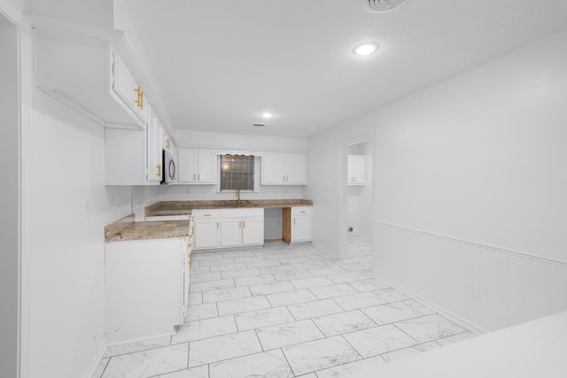kitchen featuring light countertops, stainless steel microwave, marble finish floor, recessed lighting, and white cabinetry