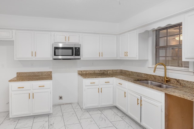 kitchen with white cabinets, light stone counters, a sink, marble finish floor, and stainless steel microwave