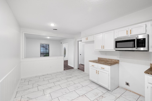 kitchen with stainless steel microwave, white cabinetry, and marble finish floor