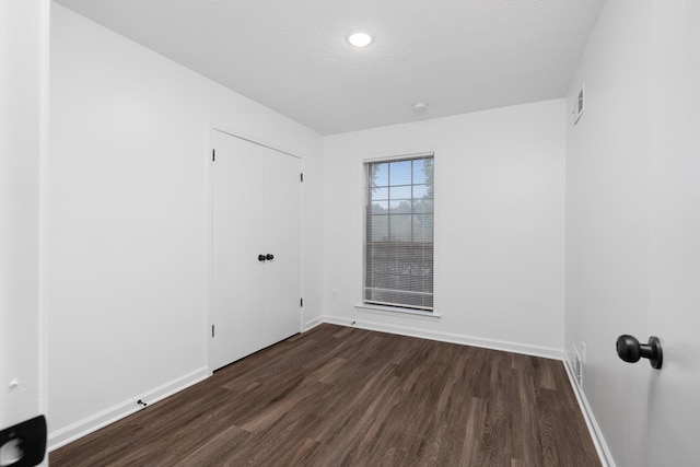 spare room featuring a textured ceiling, baseboards, visible vents, and dark wood-style floors