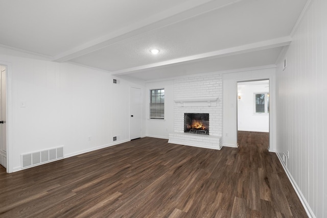 unfurnished living room with a brick fireplace, dark wood-style flooring, beamed ceiling, and visible vents