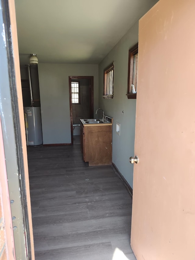 corridor with baseboards, a sink, dark wood finished floors, and water heater
