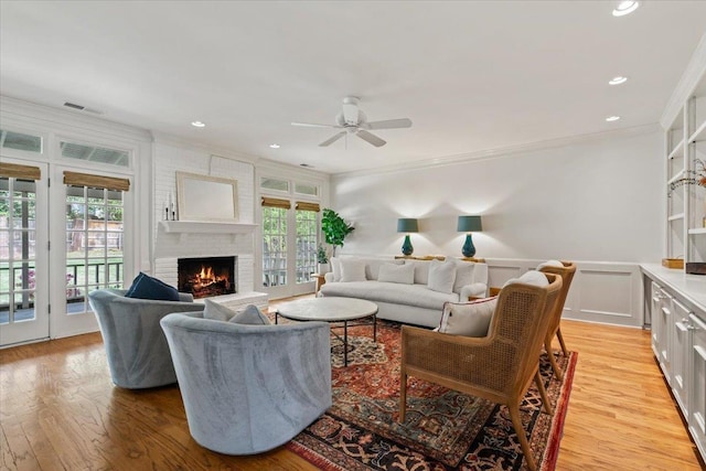 living area featuring ceiling fan, a fireplace, a wealth of natural light, visible vents, and ornamental molding