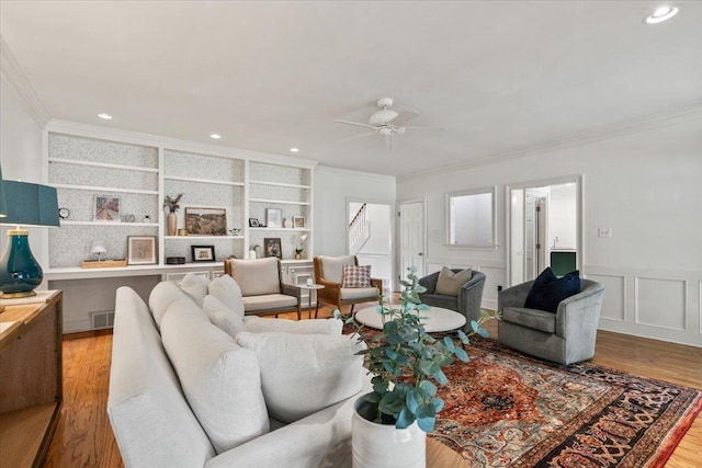 living area featuring crown molding, built in shelves, a ceiling fan, and wood finished floors