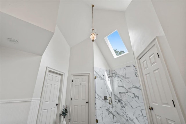 bathroom featuring a skylight, a marble finish shower, and high vaulted ceiling