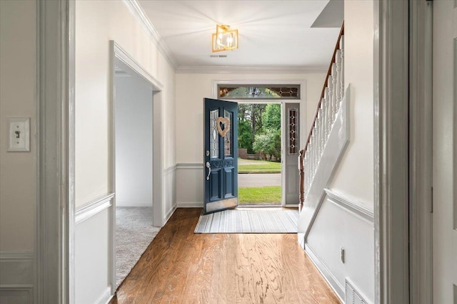 entryway with crown molding, wood finished floors, visible vents, and stairway