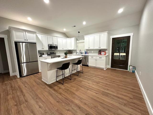50 Melrose Cv, Savannah, TN 38372 - kitchen featuring a breakfast bar area, a center island, wood finished floors, stainless steel appliances, and white cabinetry
